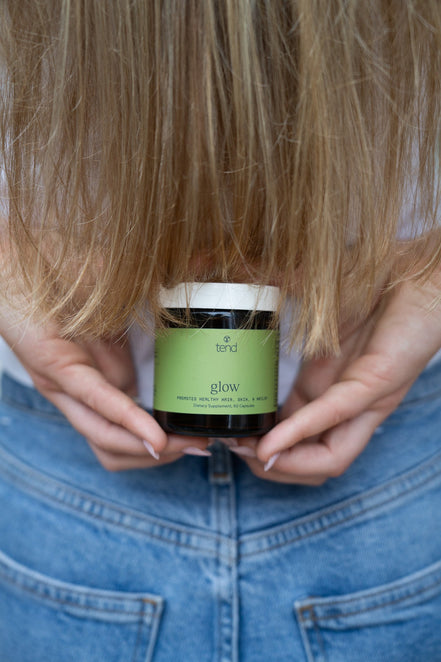 Tend Glow supplement bottle held in hand with long hair in background