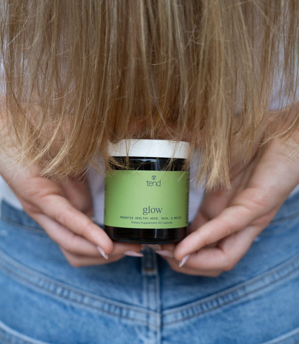 Tend Glow supplement bottle held in hand with long hair in background